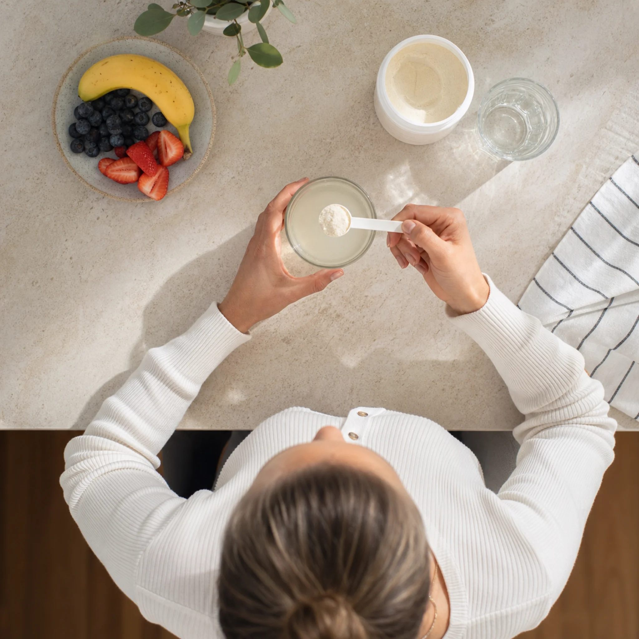 Person preparing morning collagen supplement drink by scooping powder into a ceramic mug